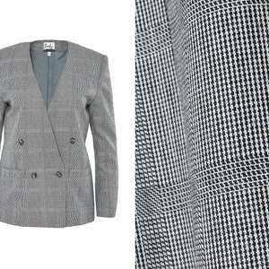 May include: A gray blazer with a black and white houndstooth pattern. The blazer has a double-breasted closure with two buttons and two flap pockets.