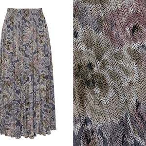May include: A long, flowing skirt with a floral pattern in shades of gray, pink, and olive green. The skirt has a pleated design and a wide waistband. The fabric has a subtle texture, and a close-up shows a herringbone weave.