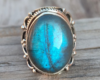 May include: A silver ring with a large oval blue labradorite gemstone. The ring has a detailed silver band.
