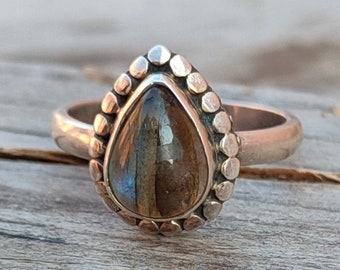 May include: A silver ring with a teardrop-shaped labradorite gemstone set in a beaded bezel.