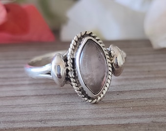 May include: A silver ring with a light pink gemstone set in a marquise shape. The ring has a delicate, ornate design with small silver accents.