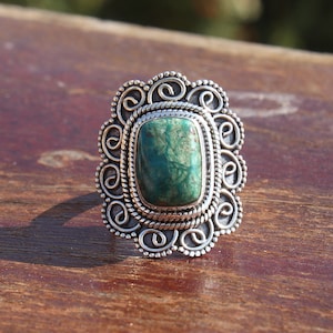 May include: A silver ring with a green gemstone set in a decorative filigree design.