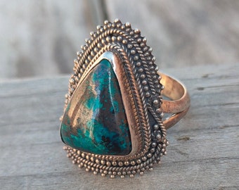 Puede incluir: Un anillo de plata con una piedra turquesa triangular engastada en un engaste de plata. El anillo tiene un borde decorativo de pequeñas cuentas de plata.