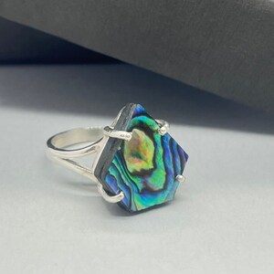 May include: A silver ring with a blue, green, and gold abalone shell set in a square shape.