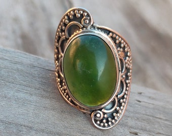 May include: A silver ring with an oval green gemstone set in a detailed filigree design.