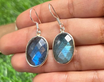 May include: A pair of silver dangle earrings with oval-shaped labradorite gemstones. The gemstones have a dark blue and green iridescent sheen.