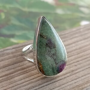 May include: A teardrop-shaped ring with a green and pink gemstone set in a silver band.