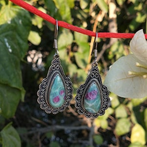 Puede incluir: Un par de pendientes de plata con gotas de piedras preciosas verdes y rosas. Los pendientes tienen un delicado diseño de filigrana.