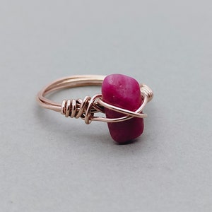 May include: A rose gold ring with a pink gemstone wrapped in wire.