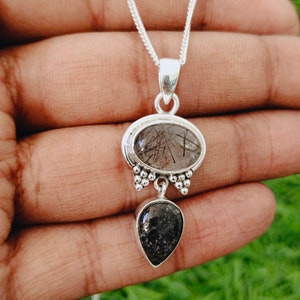 May include: Silver chain necklace with a pendant featuring two clear quartz stones. The top stone is oval-shaped with black inclusions, and the bottom stone is teardrop-shaped.