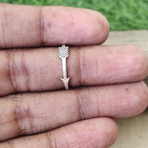 Può includere: Un anello d'argento con un design a forma di freccia. La freccia punta a destra.