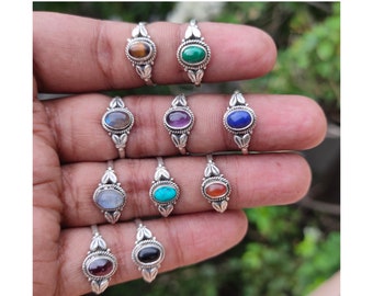 May include: A set of ten silver rings with different colored gemstones. The rings are all oval shaped and have a simple design with two small leaves on each side of the stone. The stones are: tiger's eye, malachite, labradorite, amethyst, lapis lazuli, moonstone, turquoise, carnelian, garnet, and onyx.