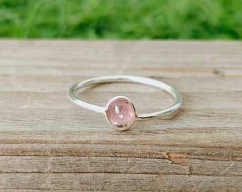 May include: A delicate silver ring with a pink oval gemstone set in the center.