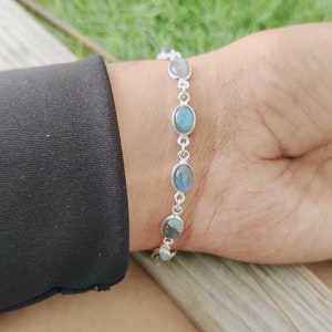 May include: A silver bracelet with oval-shaped labradorite gemstones. The bracelet is on a person's wrist.
