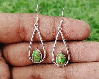 May include: Silver teardrop earrings featuring a green and brown stone. The earrings have a simple, elegant design with a hook closure. The earrings are displayed against a green background.