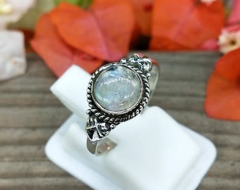 May include: A silver ring with a round, iridescent moonstone set in a decorative silver band.
