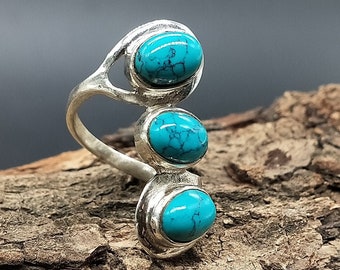 May include: A silver ring with three turquoise stones set in a vertical line. The stones are oval shaped and have a mottled blue and green color.