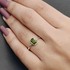 May include: A silver ring with a green gemstone. The gemstone is rectangular and has a faceted cut.