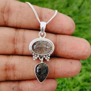 May include: A silver necklace with a pendant featuring two black and clear quartz stones. The top stone is oval-shaped and the bottom stone is teardrop-shaped.