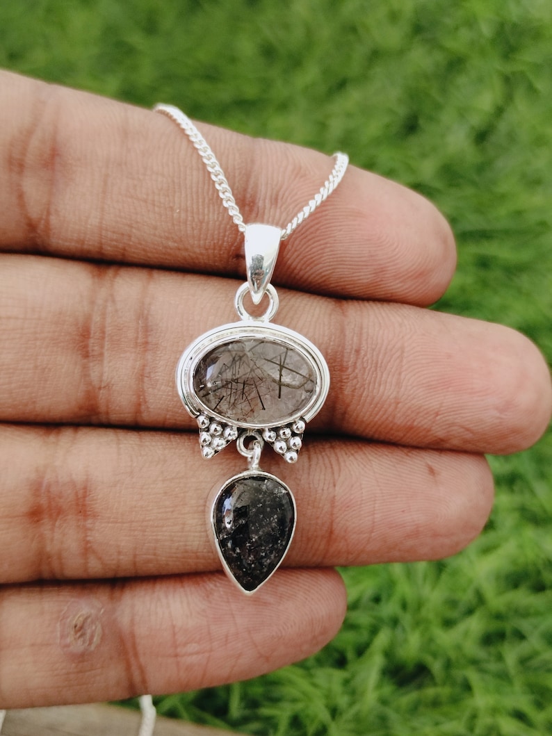 May include: A silver necklace with a pendant featuring two black and clear quartz stones. The top stone is oval-shaped and the bottom stone is teardrop-shaped.