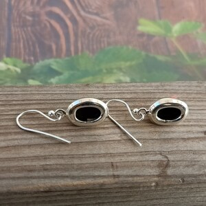 May include: A pair of silver earrings with black oval-shaped stones. The earrings have a simple design and are perfect for everyday wear.
