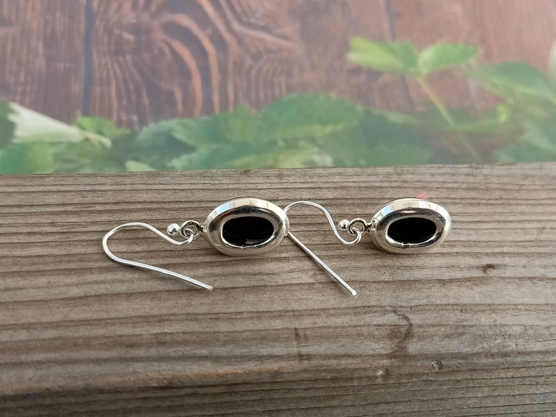 May include: A pair of silver earrings with black oval-shaped stones. The earrings have a simple design and are perfect for everyday wear.
