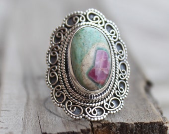 May include: A silver ring with an oval-shaped green and pink gemstone set in a filigree design.