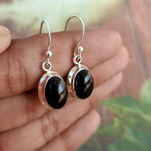 May include: A pair of silver earrings with black oval gemstones. The earrings have a simple design and are perfect for everyday wear.