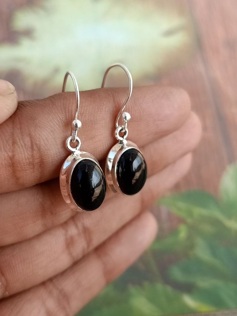 May include: A pair of silver earrings with black oval gemstones. The earrings have a simple design and are perfect for everyday wear.