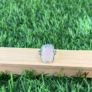 Puede incluir: Un anillo de plata con una gran piedra preciosa blanca facetada. El anillo est&aacute; sobre una superficie de madera.