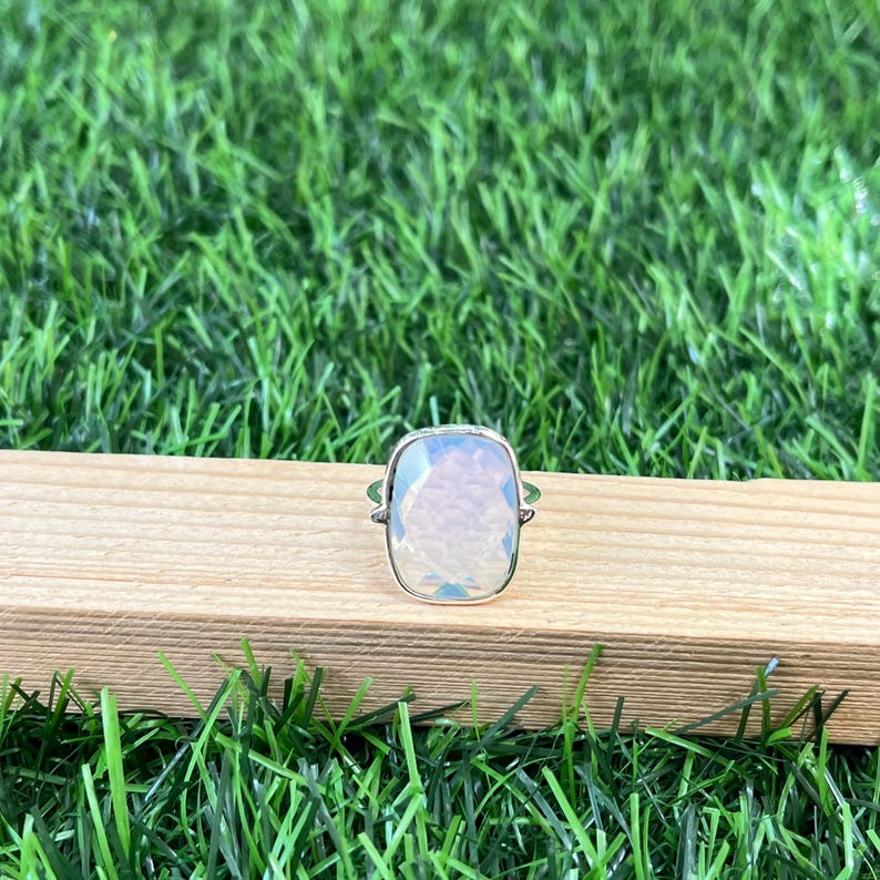 Puede incluir: Un anillo de plata con una gran piedra preciosa blanca facetada. El anillo est&aacute; sobre una superficie de madera.