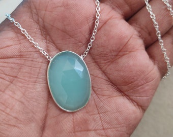 May include: A silver chain necklace with a light blue oval-shaped gemstone pendant.