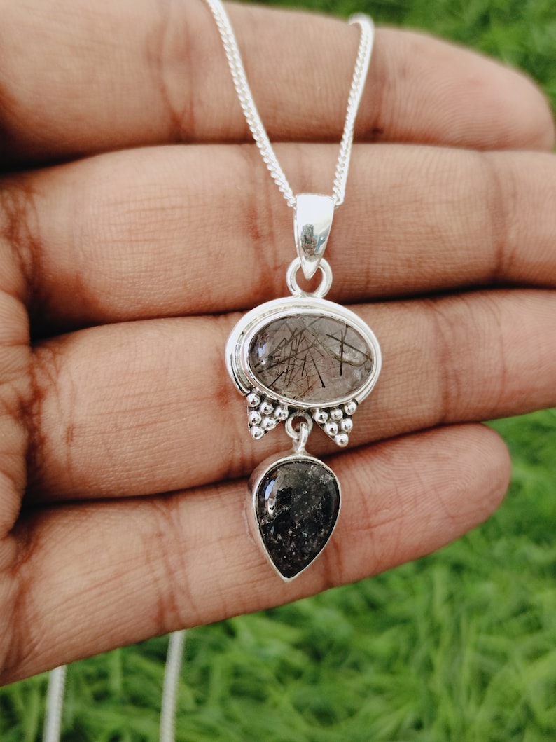 May include: Silver chain necklace with a pendant featuring two clear quartz stones. The top stone is oval-shaped with black inclusions, and the bottom stone is teardrop-shaped.