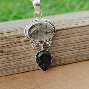 May include: Silver pendant with a clear quartz stone with black inclusions and a black teardrop-shaped stone.