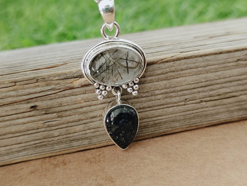 May include: Silver pendant with a clear quartz stone with black inclusions and a black teardrop-shaped stone.