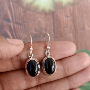 May include: A pair of silver dangle earrings with black oval gemstones.