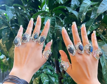 May include: A set of six silver rings with teardrop-shaped labradorite gemstones. The rings are worn on the fingers of two hands.