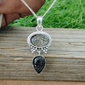 May include: A silver necklace with a black and clear crystal pendant. The pendant is made of two stones, one round and one teardrop shaped. The stones are set in silver.