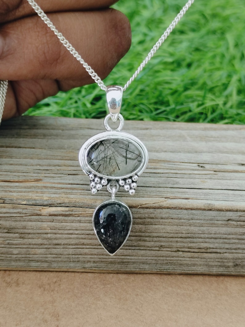 May include: A silver necklace with a black and clear crystal pendant. The pendant is made of two stones, one round and one teardrop shaped. The stones are set in silver.
