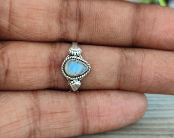 May include: A silver ring featuring a pear-shaped moonstone. The moonstone has a blue and white color. The ring has a rope-like design around the stone and decorative details on the band.