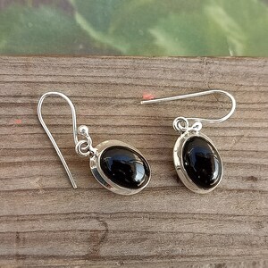 May include: A pair of silver earrings with black oval gemstones. The earrings have a simple design with a hook fastening.