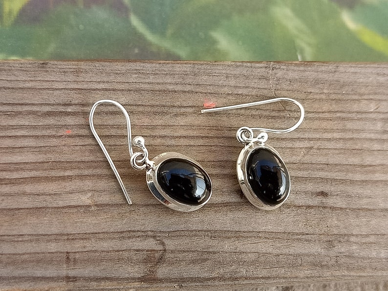 May include: A pair of silver earrings with black oval gemstones. The earrings have a simple design with a hook fastening.