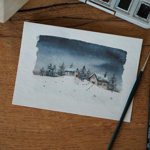 Può includere: Un dipinto ad acquerello su carta rettangolare che raffigura un paesaggio invernale innevato con due piccole case e diversi pini sotto un cielo notturno scuro e suggestivo. La scena presenta neve bianca soffice e toni blu scuri.