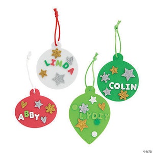 May include: Four foam Christmas ornaments with string hangers. The ornaments are white, red, green, and have glitter and foam shapes. The ornaments have the names Abby, Linda, Colin, and Lydiy written on them.