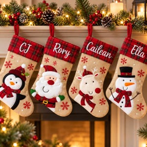 May include: Four beige Christmas stockings with red tartan cuffs, each personalised with the names CJ, Rory, Cailean, and Ella. The stockings feature embroidered red snowflakes and appliqued characters: a penguin, Santa Claus, a reindeer, and a snowman.