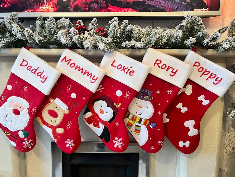 Pode incluir: Cinco meias de Natal vermelhas com punhos brancos, bordadas com os nomes Daddy, Mommy, Loxie, Rory e Poppy. As meias apresentam desenhos aplicados do Pai Natal, uma rena, um pinguim, um boneco de neve e formas de ossos brancos.