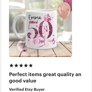 May include: White ceramic mug with the text "Emma 50 & Fabulous" in pink glitter lettering. The mug has a handle and a crown design above the number 50. Two balloons are in the background.