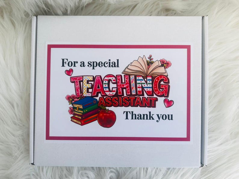 May include: A white box with a pink border featuring the text "For a special TEACHING ASSISTANT Thank you." The word "TEACHING" is in a colorful, patterned font. The image includes illustrations of books, flowers, and an apple.