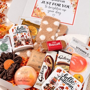 May include: A gift box containing a white mug and square coaster with hello autumn text, tan polka dot socks, a Lamai Beauty honey and almond bath fizzer, a brown scrunchie, an orange tea light, Biscoff biscuit, Galaxy chocolate, and Vitamin C face mask.