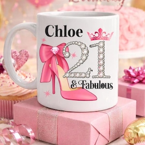 May include: White ceramic mug with the name "Chloe", the number "21" in rhinestones, and the words "& Fabulous". The mug features a pink high heel, bow, and crown design. The mug is sitting on a pink gift box.